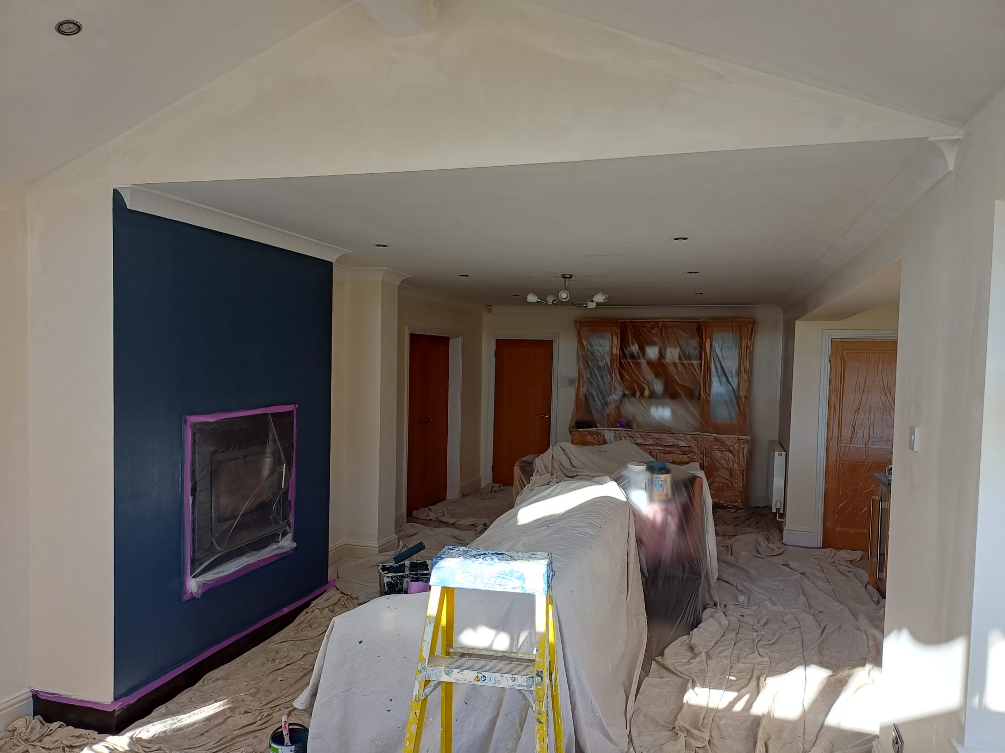 Private sitting room being painted, navy chimney breast, dust sheets and a stepladder