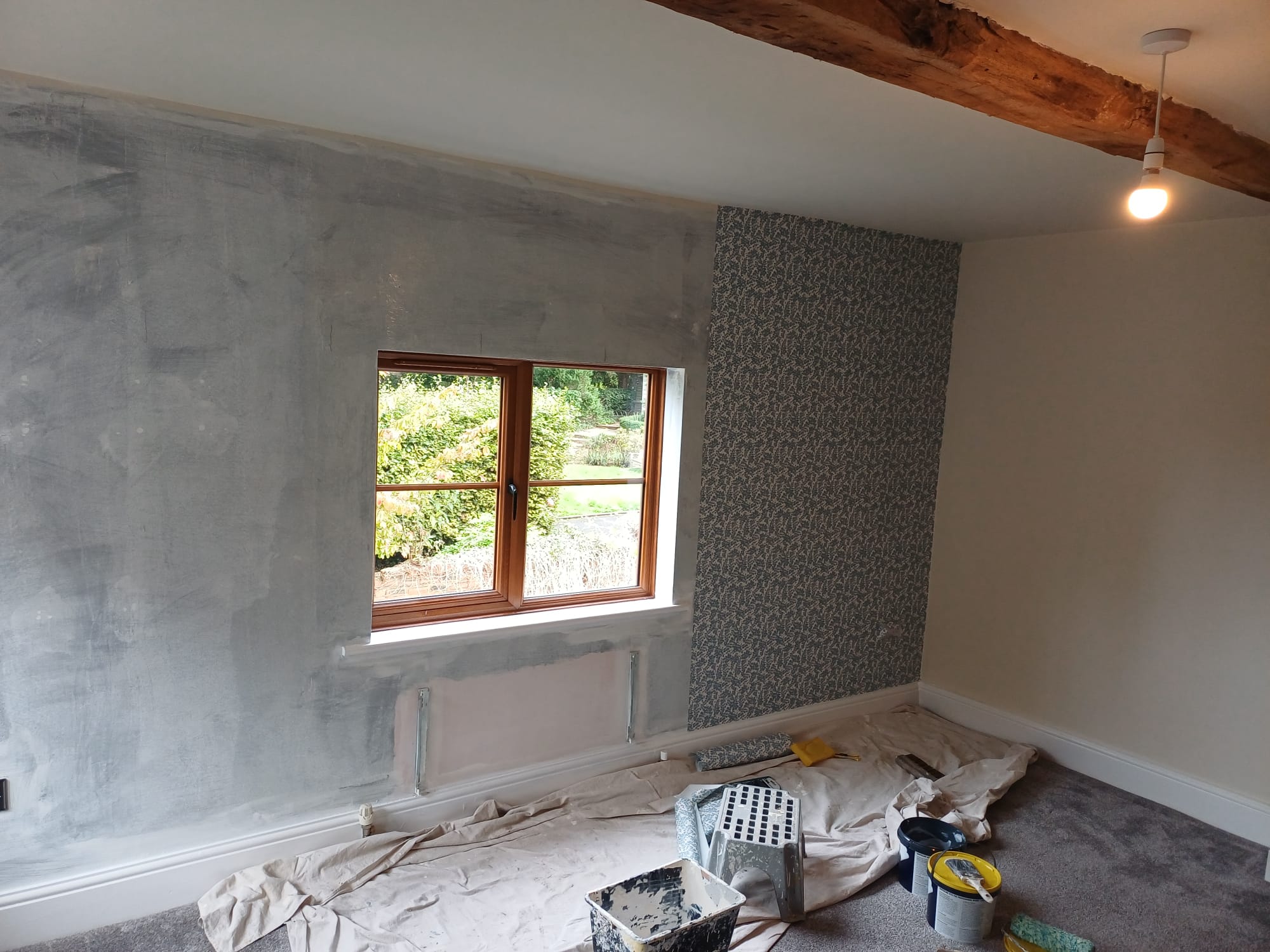 Wallpaper being hung beside a prepared wall, dust sheets and paste on the floor